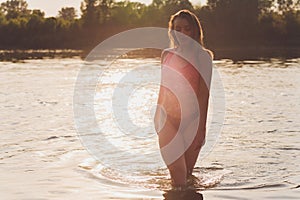 Portrait of young woman swimsuit is standing in the water in a forest lake in the sunset.