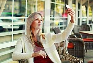 Portrait young woman taking selfie picture by smartphone sitting at a table in a cafe