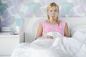 Portrait of young woman taking temperature with thermometer photo