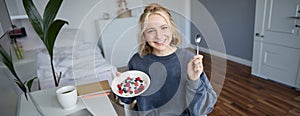 Portrait of young woman talking to audience, recording vlog on digital camera, showing her breakfast, talking about