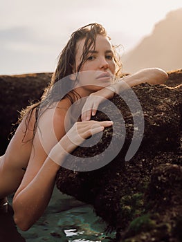 Portrait of young woman with tanned body on ocean beach. Beauty lady look at camera in water with warm sunlight