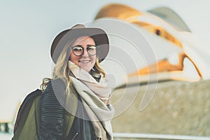 Portrait of young woman tourist with backpack. Girl is standing on city street. In background is modern building