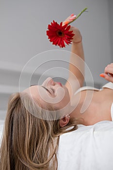 portrait of young woman in underwear on bed. holding red pink flower. female in a hotel room or home. white bedroom and