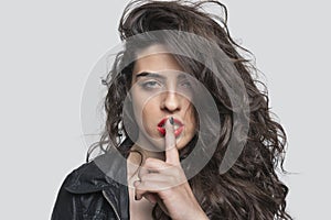 Portrait of a young woman with unkept hair and finger on lips against gray background photo