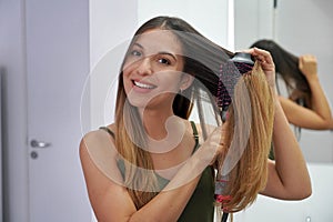 Portrait of young woman using round brush hair dryer to style hair in an easy way at home. Girl with electric blowout brush hair