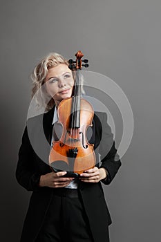 Portrait of an young woman violinist in a black male suit with a violin looking up