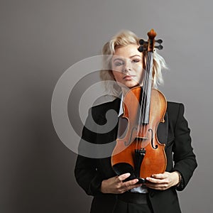Portrait of an young woman violinist in a black male suit with a violin