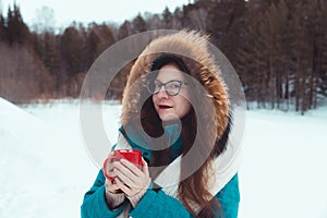 Portrait of young woman in warm coat with cup of hot chocolate on the snowy field. Winter nature. Selective focus