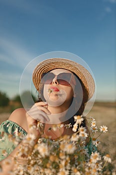 Portrait of young woman wearing canotier hat, green dress and sunglasses with flower in her hands in daisy field photo