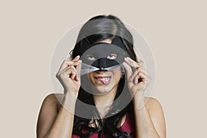 Portrait of a young woman wearing eye mask while biting lip over colored background