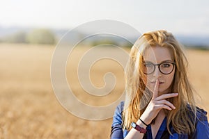 Young woman is gesturing Shhh in corn field