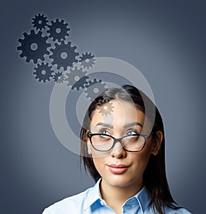 Portrait of young woman wearing glasses looking up at cogwheels isolated on grey background