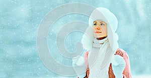 Portrait of young woman wearing hat, sweater and scarf on snowy forest background with snowflakes