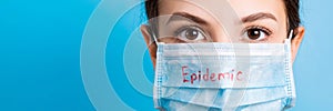 Portrait of young woman wearing medical mask with epidemic word at blue background. Protect your health. concept