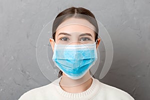 Portrait of young woman wearing medical mask at gray cement background. Person is happy because she is finally healthy. Protect