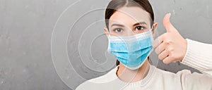 Portrait of young woman wearing medical mask at gray cement background. Person is happy because she is finally healthy. Protect