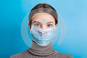 Portrait of young woman wearing medical mask with MERS word at blue background. Protect your health. concept