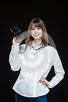 Portrait of a young woman wearing a white shirt holding a camera in her hand. The concept of a successful photographer