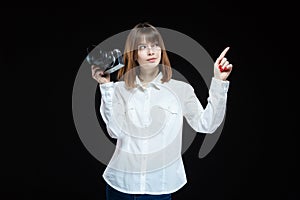 Portrait of a young woman wearing a white shirt, holding a camera in her hand and pointing with her hand at your text