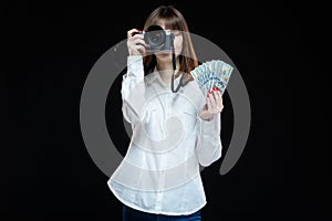 Portrait of a young woman wearing a white shirt holding a camera and US dollars in her hand. The concept of a successful