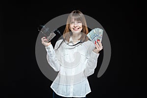 Portrait of a young woman wearing a white shirt holding a camera and US dollars in her hand. The concept of a successful