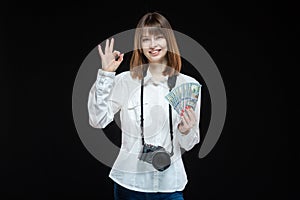 Portrait of a young woman wearing a white shirt holding a camera and US dollars in her hand. The concept of a successful