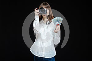 Portrait of a young woman wearing a white shirt holding a camera and US dollars in her hand. The concept of a successful