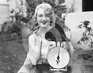 Portrait of a young woman weighing her puppy on a weighing scale