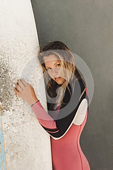 portrait of young woman in wetsuit with surfing board against