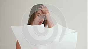 Portrait of young woman in white being tired, trying to throw stack of blueprints on paper out of frustration. Girl