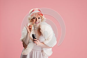 Portrait of young woman in white dress on coral pink background. Female model as a legendary actress. Pin up. Concept of