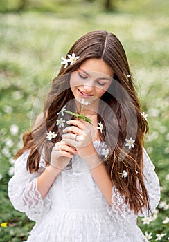 Portrait of a young woman in a white dress with primroses. A girl in the spring forest. White anemones in long brown hair