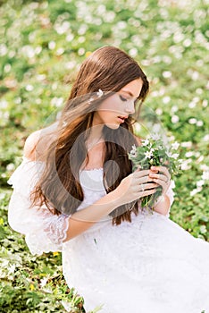 Portrait of a young woman in a white dress with primroses. A girl in the spring forest. White anemones in long brown hair