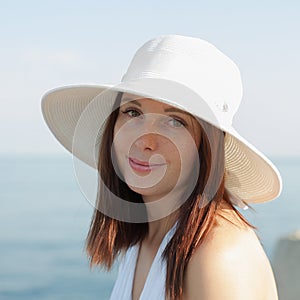 Portrait of young woman in white hat against sea