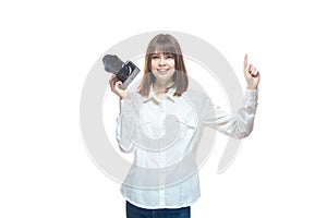 Portrait of a young woman in a white shirt, holding a camera in her hand and pointing her finger at the information. The