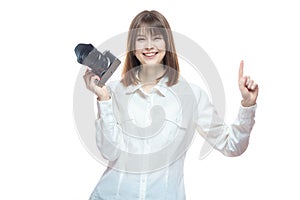 Portrait of a young woman in a white shirt, holding a camera in her hand and pointing her finger at the information. The