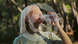 Portrait of a young woman who drinks clear water from a bottle in the forest
