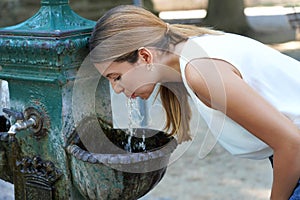 Portrait of young woman who hydrates herself drinking water from a fountain during heat wave on summer photo