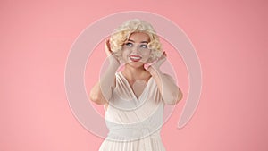 Portrait young woman in wig, white dress and with red lipstick on lips in studio on pink background. Woman looking like