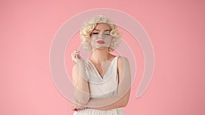 Portrait young woman in wig, white dress and with red lipstick on lips in studio on pink background. Woman looking like