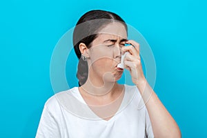 Portrait of a young woman wincing when using an inhaler. Blue background. Copy space photo