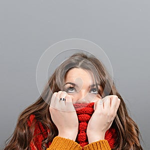 Portrait of young woman in winter clothes looking up against gray background