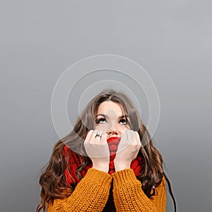 Portrait of young woman in winter clothes looking up against gray background