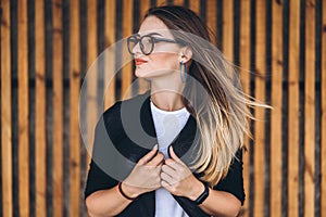 Portrait of a young woman on the wooden background with vertical boards. Beautiful girl with long hair and glasses smiling