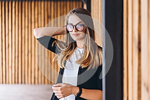 Portrait of a young woman on the wooden background with vertical boards. Beautiful girl with long hair and glasses smiling