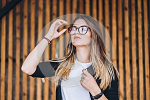 Portrait of a young woman on the wooden background with vertical boards. Beautiful girl with long hair and glasses smiling