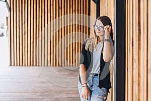 Portrait of a young woman on the wooden background with vertical boards. Beautiful girl with long hair and glasses smiling