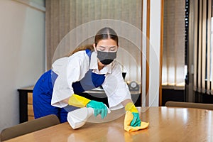 Portrait of a young woman worker in a protective mask, washing an office desk