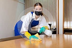 Portrait of a young woman worker in a protective mask, washing an office desk