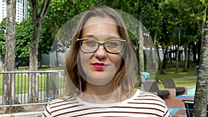 Portrait of young woman in yellow glasses and earpieces listening to music
